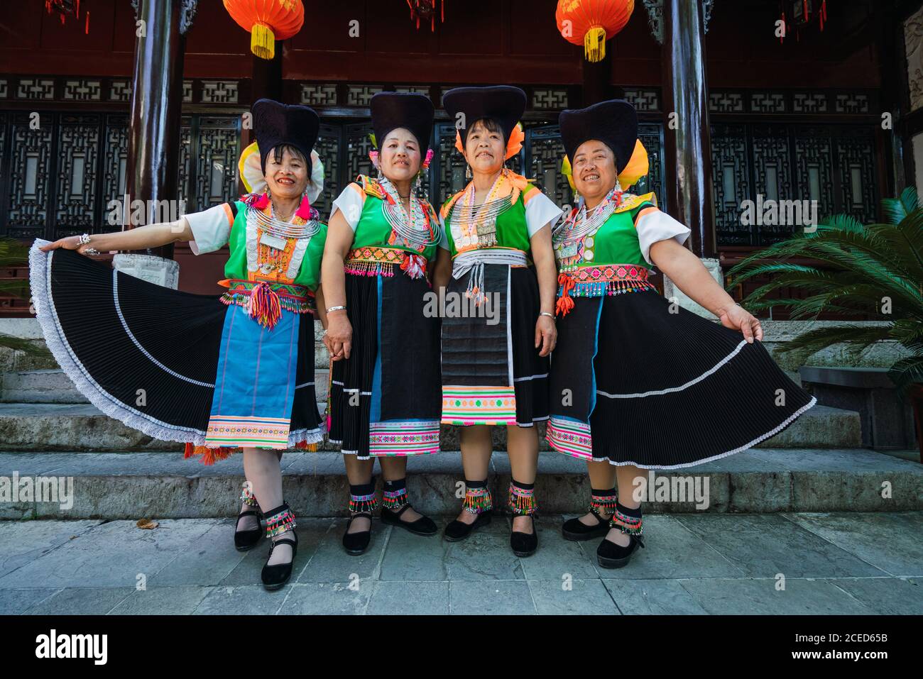 GUINZHOU, CINA - 14 GIUGNO 2018: Gruppo di belle donne cinesi della minoranza Miao che si trova in un edificio tradizionale in abiti da festival luminosi con ornamenti che tengono gonne e che guarda sorridente nella provincia di Guizhou Foto Stock