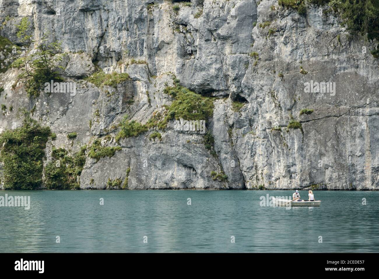 Coppia in una barca a remi sul lago Koenigssee godendo pittoresco scenario di fronte all'enorme parete rocciosa Foto Stock