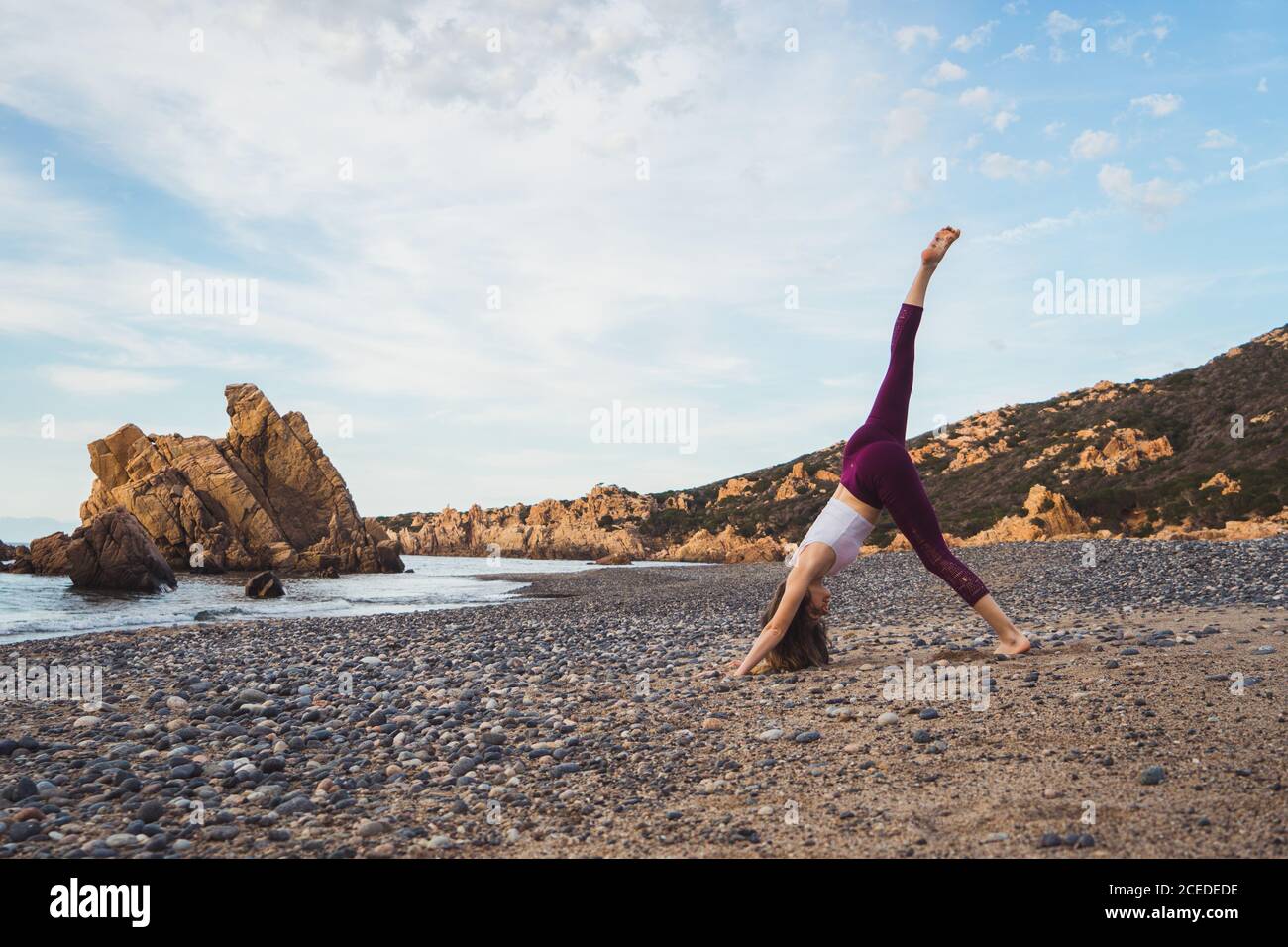 Vista laterale della donna sportiva in piedi con la gamba in su e praticare yoga sulla riva dell'oceano. Foto Stock