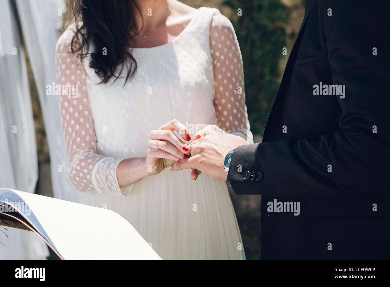 Crop vista di sposa giovane in abito da sposa e sposo in costume nero scambiando anelli alla cerimonia in giardino Foto Stock