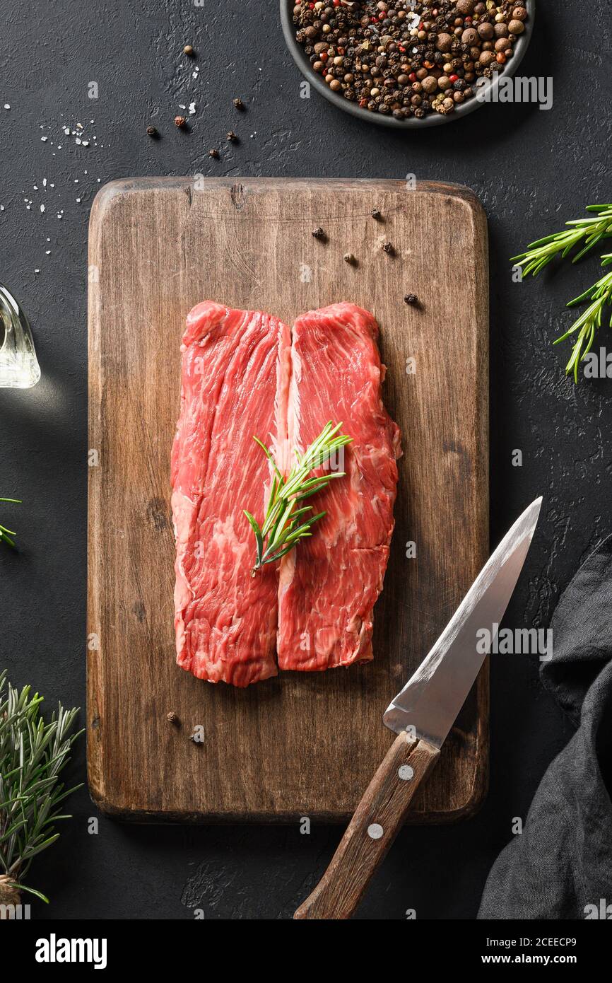 Bistecca di ribeye marmorizzata cruda con sprig di rosmarino sul tagliere. Composizione verticale. Foto Stock