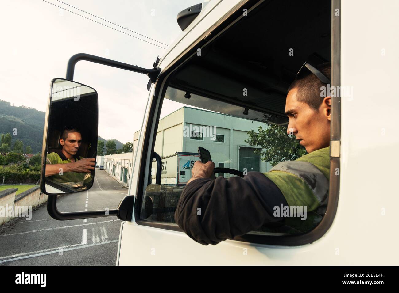 Giovane uomo nel suo camion all'interno della cabina con il indumenti di sicurezza con lo smartphone Foto Stock