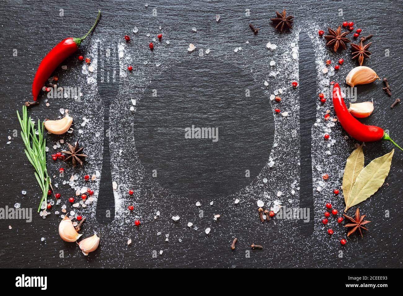 Varie erbe e spezie su tavola di pietra scura. Posate silhouette su tavola nera con sale, spezie, peperoncino, rosmarino e aglio. Foto Stock