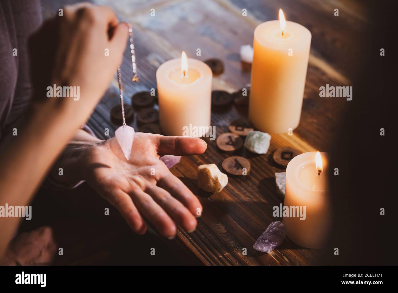 Libra con un pendolo sopra la mano, guarigione o oracolo foretelling, candele, rune e pietre di guarigione Foto Stock