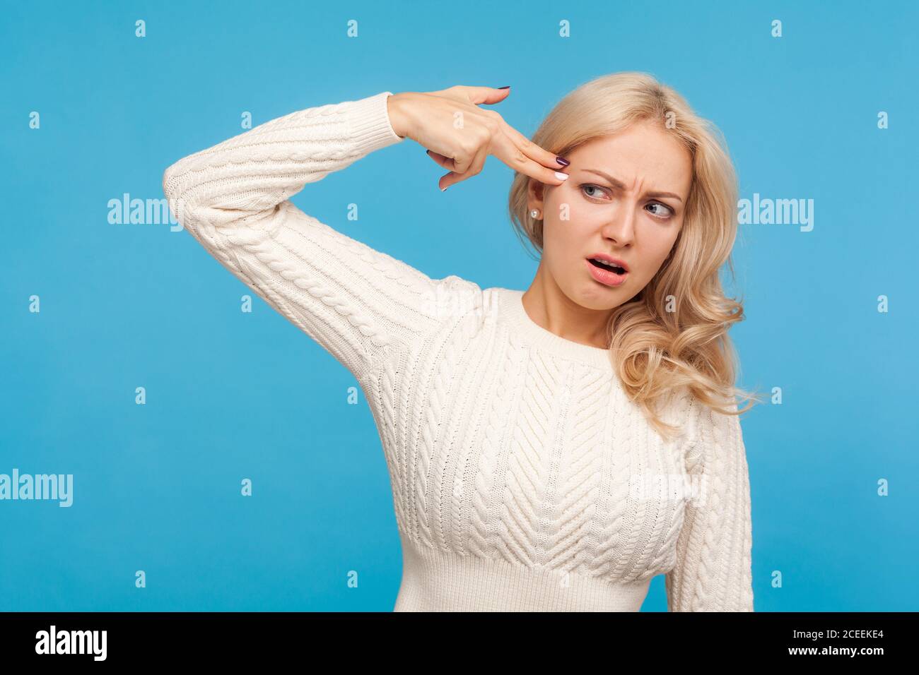 Sconvolto stanco di vita bionda donna che tiene le dita vicino alla testa imitando pistola, desiderio di commettere suicidio, isteria, problemi nella vita. Studio interno con isol di ripresa Foto Stock