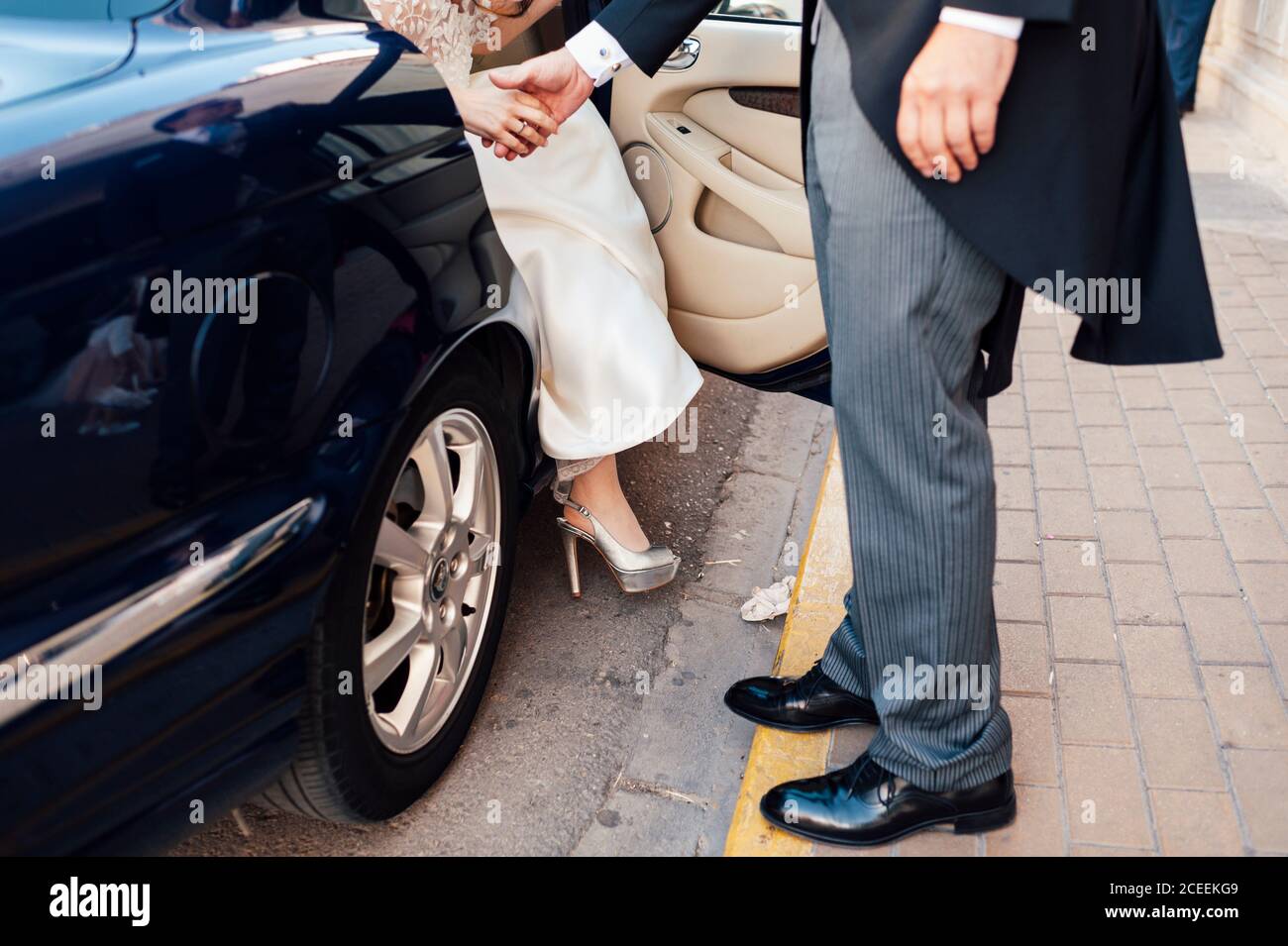 Crop uomo in tuta aiutare a sposa a uscire di auto nera. Foto Stock