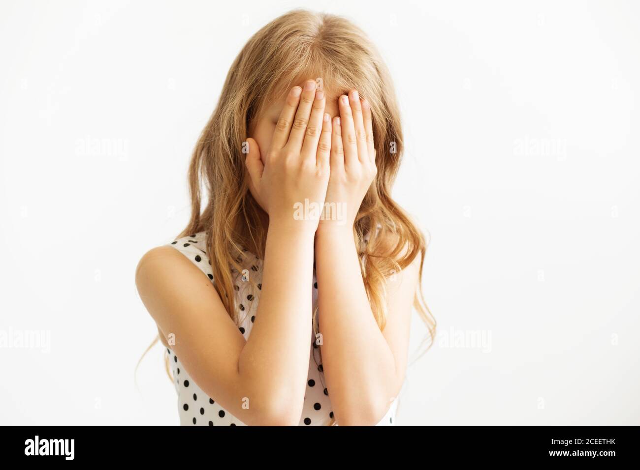 Bambino che copre il volto con le mani. La bionda bambina si copre la  faccia con le sue mani isolato. Ragazza nascondere la faccia sotto le mani,  a giocare a nascondino Foto