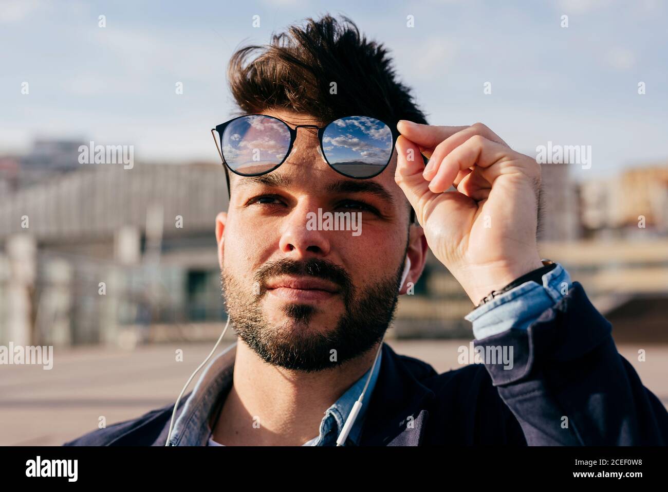 La testa dell'uomo alla moda con la bearded con la pettinatura usando le  cuffie e togliendo gli occhiali da sole guardando via alla luce del sole  Foto stock - Alamy