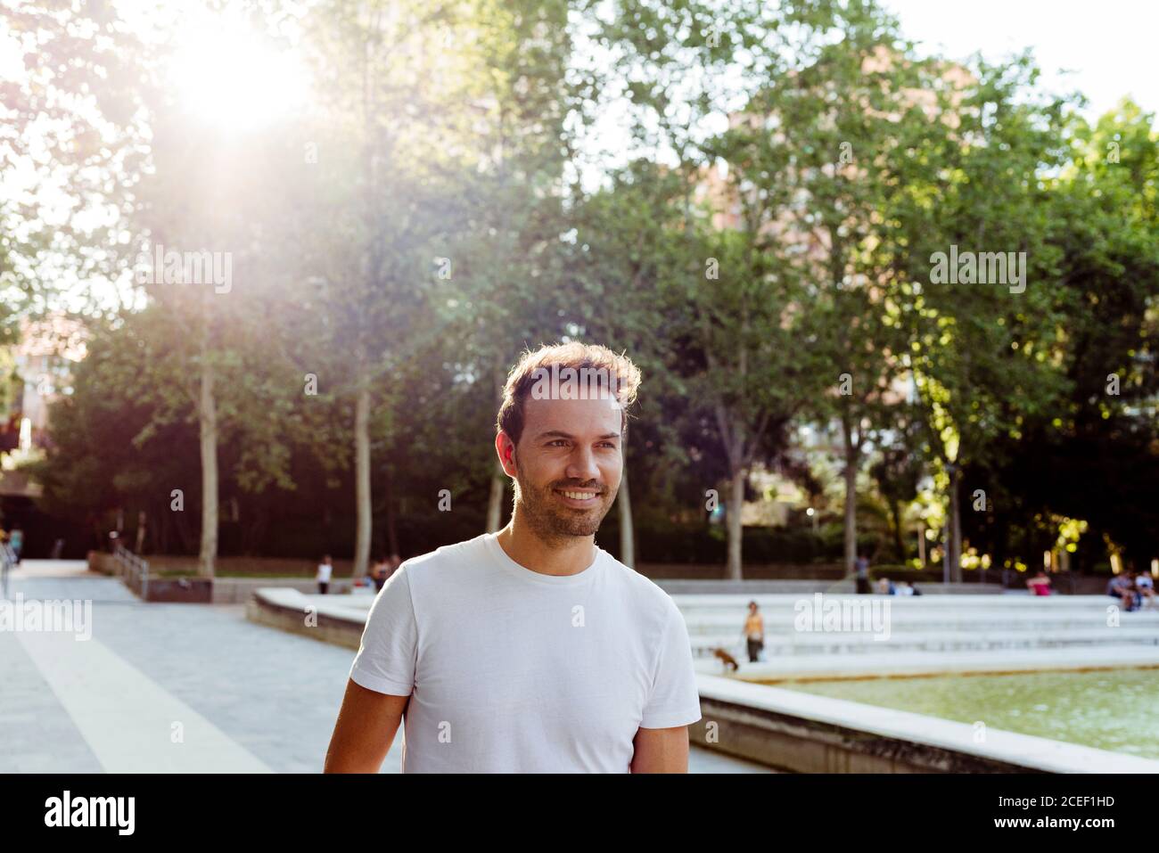 Bel ragazzo in T-shirt bianca sorridente e a piedi parcheggia il giorno di sole Foto Stock