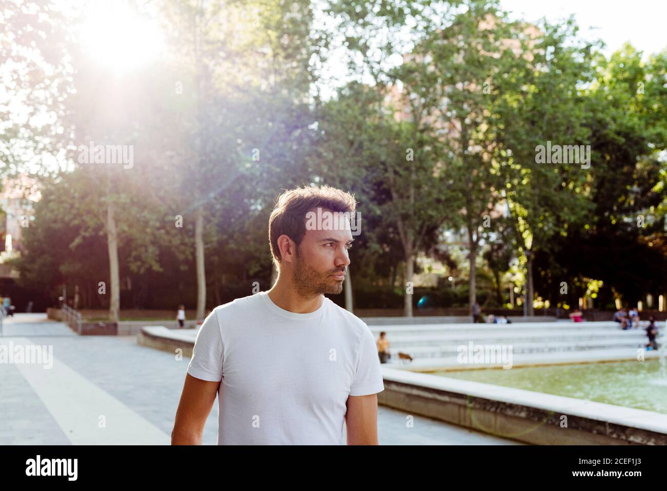 Bel ragazzo in T-shirt bianca sorridente e a piedi parcheggia il giorno di sole Foto Stock