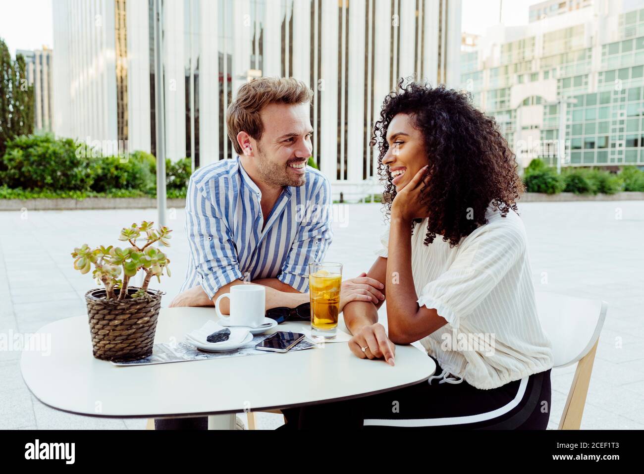 Bella afro-americana donna e bel caucasico uomo sorridendo e guardando l'un l'altro mentre si passa il tempo in caffè all'aperto insieme Foto Stock