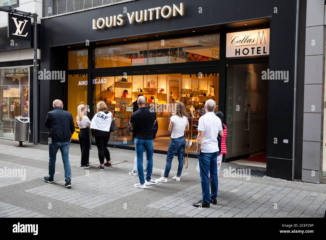 Per rispettare le norme sulla distanza durante la pandemia di Corona, i clienti stanno aspettando di fronte al negozio Louis Vuitton sulla via dello shopping Hohe St Foto Stock
