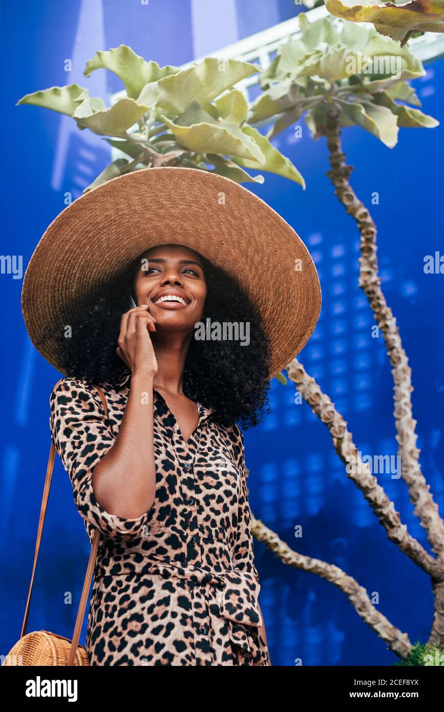 Donna con un cappello di paglia che cammina in una bella architettura parlare sul telefono cellulare Foto Stock