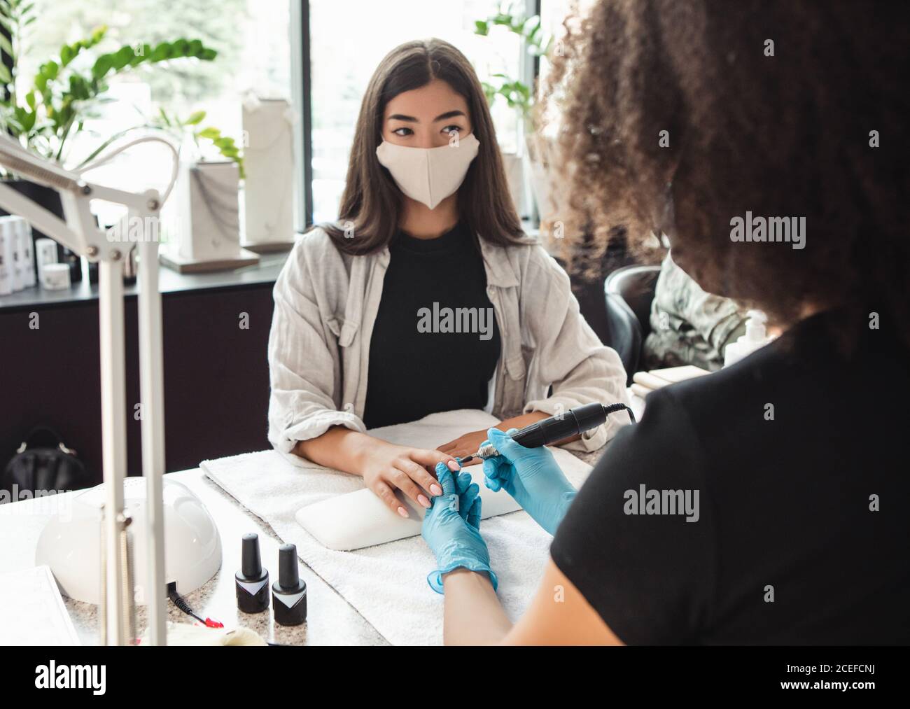 Lavoro di manicure e pedicure salone. Asian ragazza guarda master in maschera protettiva durante la procedura elettrica unghia Foto Stock