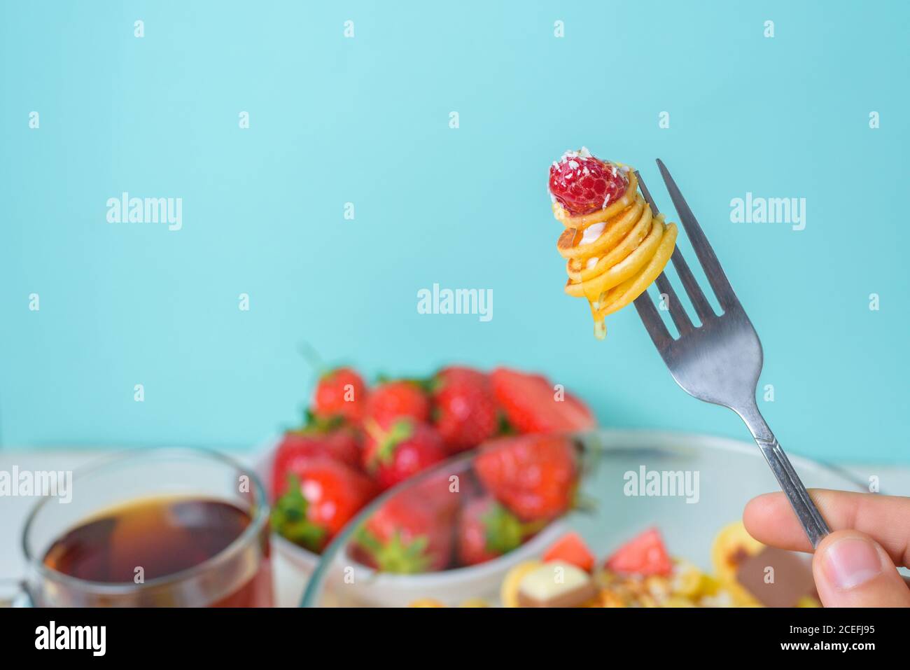 minuscoli pancake su una forchetta con fragole fresche, banana, cioccolato, patatine di cocco e miele in un piatto su sfondo blu. tendenza alimentare 2020. Foto Stock