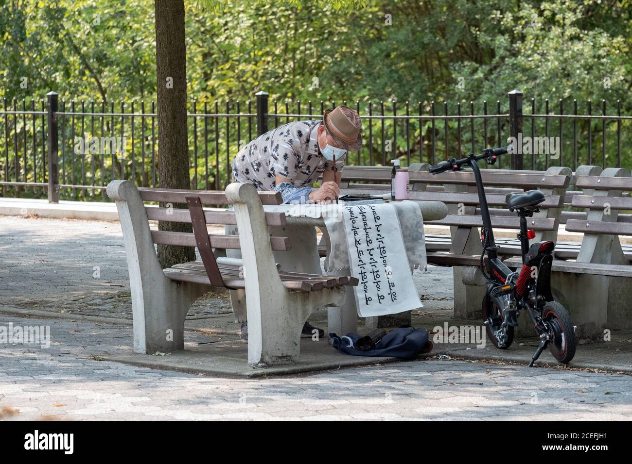 AREA DI LAVORO. Un calligrafo americano coreano scrive i versi della bibbia su una pagina sottile lunga da usare come decorazioni domestiche. All'aperto in un parco a Queens, New York Foto Stock