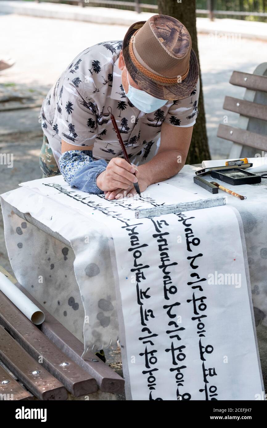 Un calligrafo americano coreano scrive i versi della bibbia su una pagina sottile lunga da usare come decorazioni domestiche. All'aperto in un parco a Queens, New York. Foto Stock