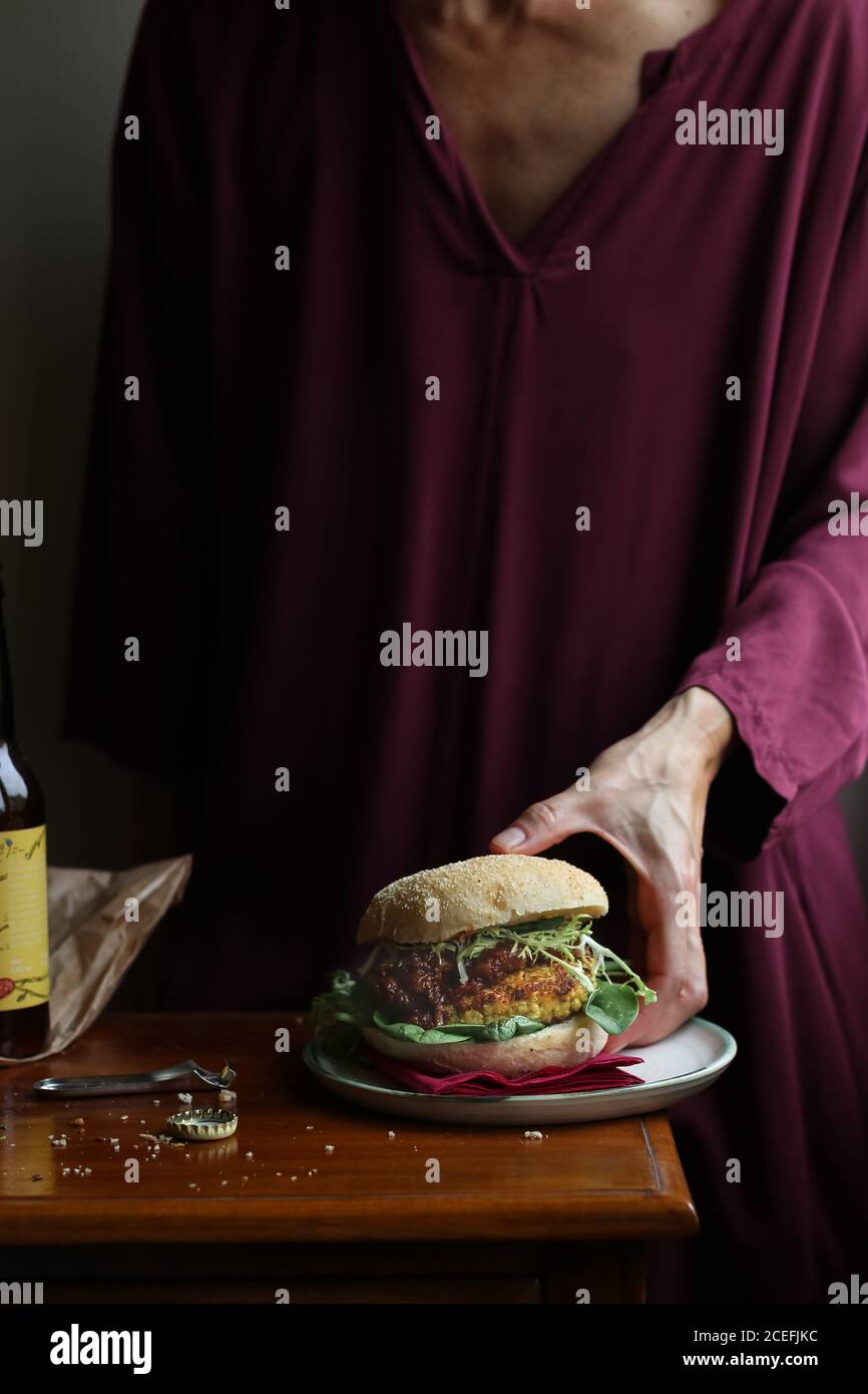 Crop Woman gustando birra e hamburger vegetariani Foto Stock