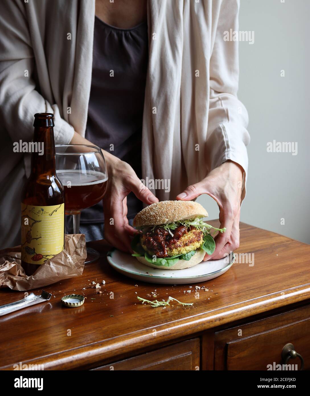 Crop Woman gustando birra e hamburger vegetariani Foto Stock