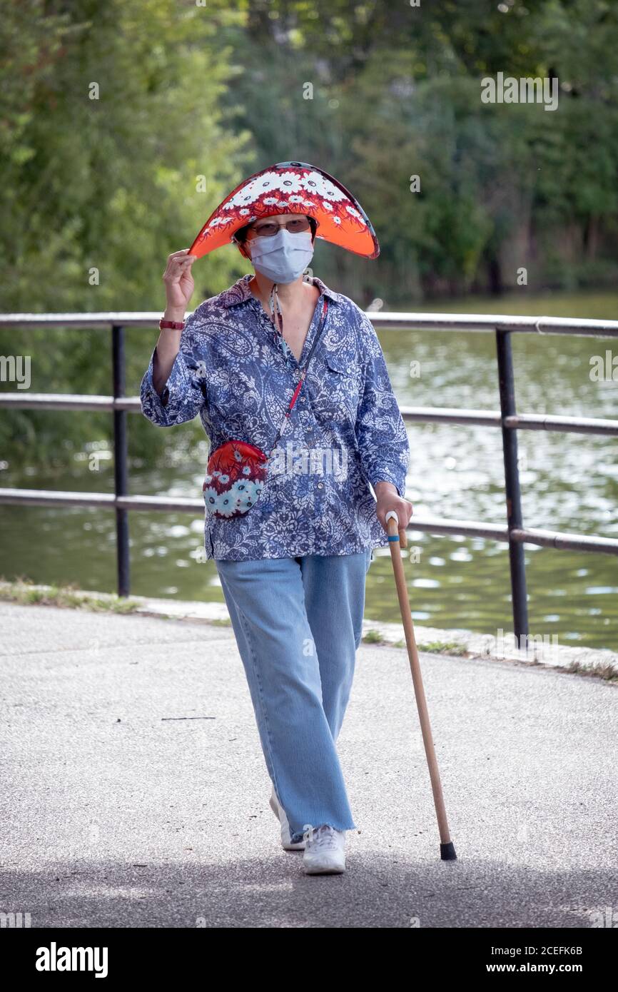 Una donna elegante nei suoi anni settanta va per una camminata di esercitazione che indossa una maschera chirurgica & cappello di corrispondenza & borsa. In un parco a Flushing, Queens, New York. Foto Stock