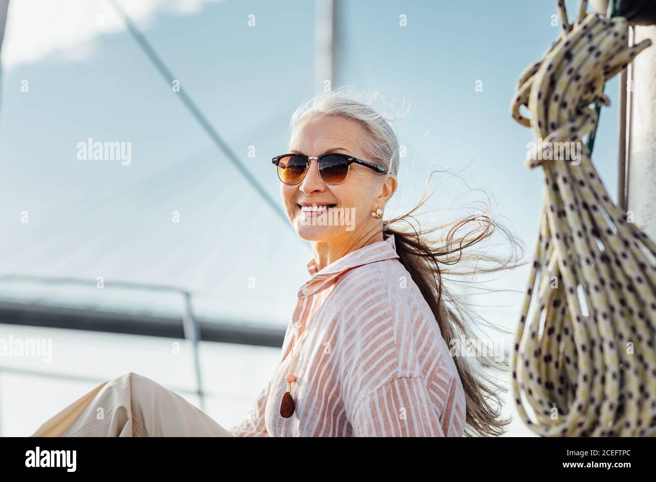 Ritratto di una donna matura felice che indossa occhiali da sole su uno yacht. Bella donna con capelli lunghi guardando la macchina fotografica mentre ti godi una gita in barca. Foto Stock