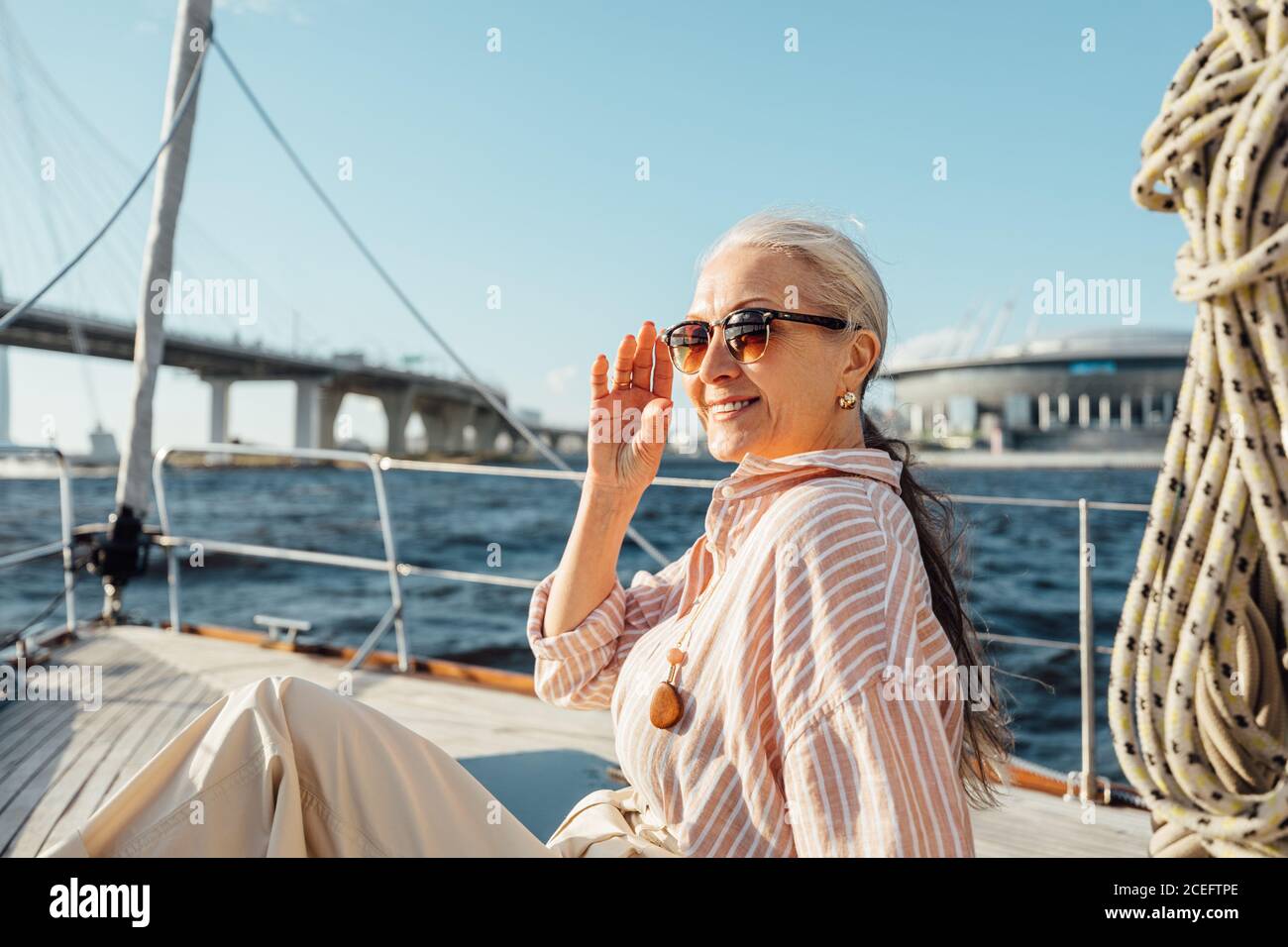 Bella donna anziana che tiene un occhiali da sole e che guarda via sopra uno yacht privato Foto Stock