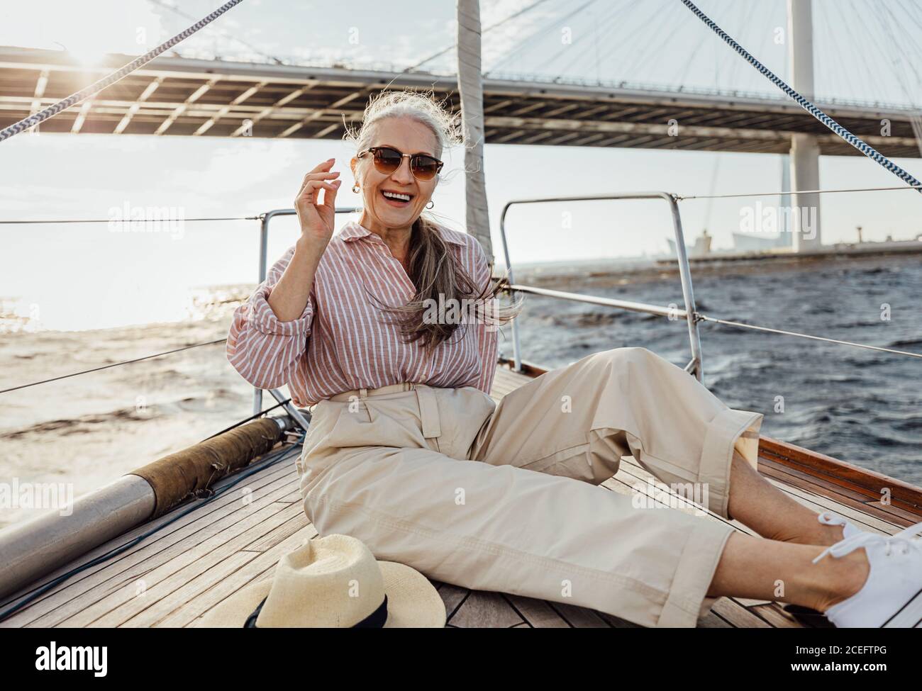 Felice donna matura che riposa su una prua yacht. Donna sorridente che si gode di una gita in barca con occhiali da sole. Foto Stock