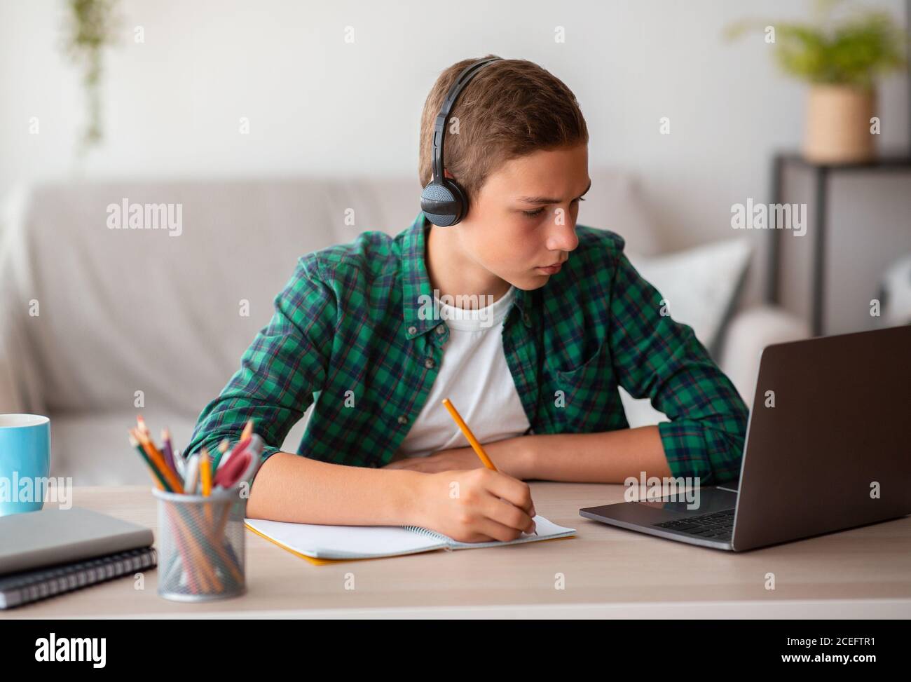 Ragazzo di scuola pensivo con gli auricolari che studia online da casa Foto Stock