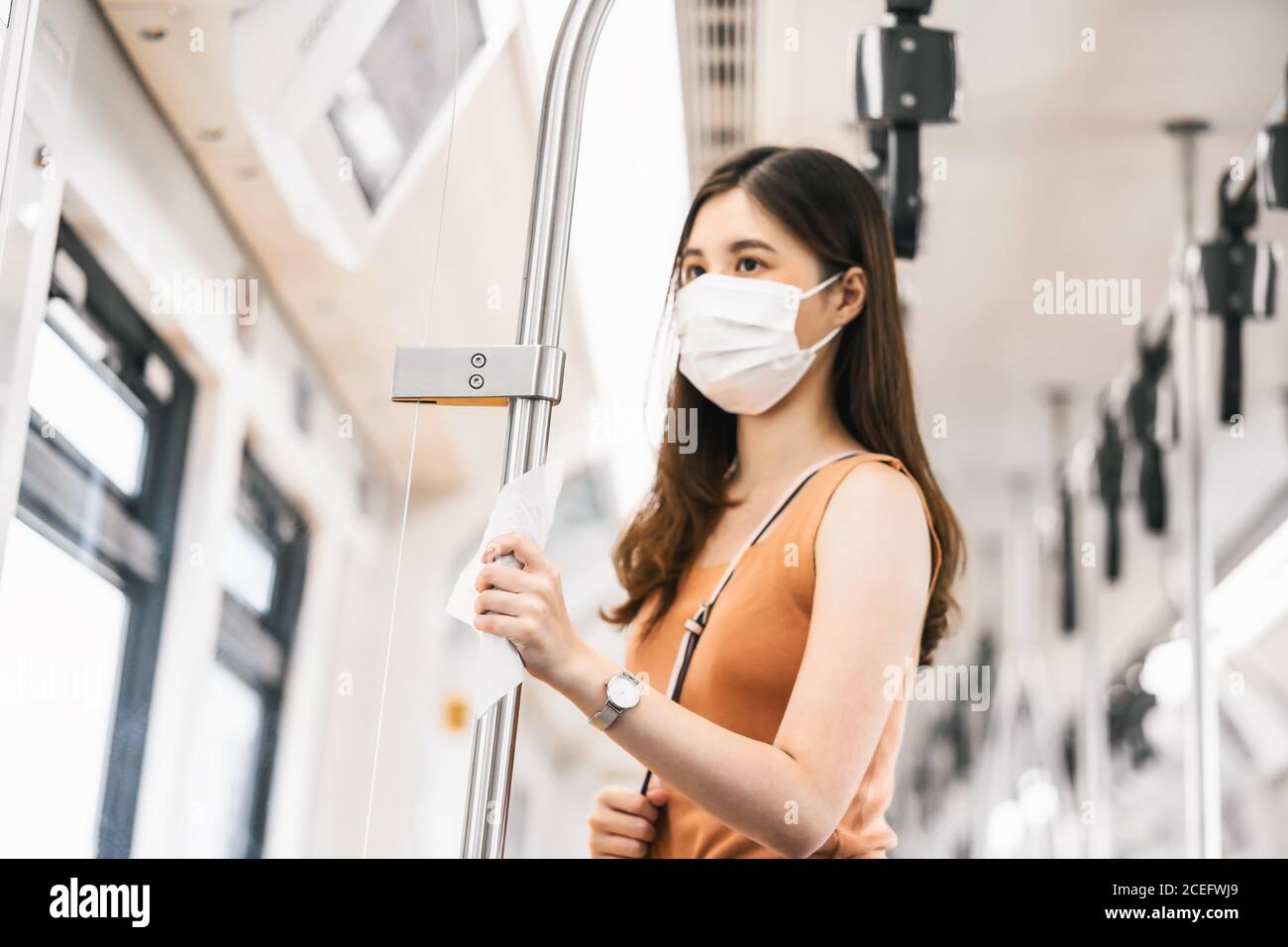 Mano closeup che tocca con wet wipe di giovane donna asiatica il passeggero indossa una maschera chirurgica nel treno della metropolitana durante il viaggio Grande città a Covid19 Outbera Foto Stock