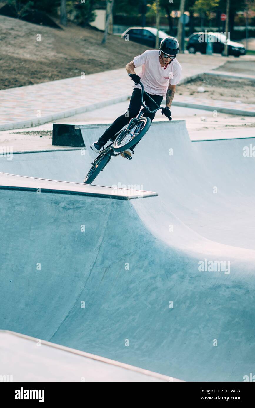 Giovane uomo in T-shirt bianca e casco su cui si monta BMX trampolino sullo sfondo di strada e auto Foto Stock