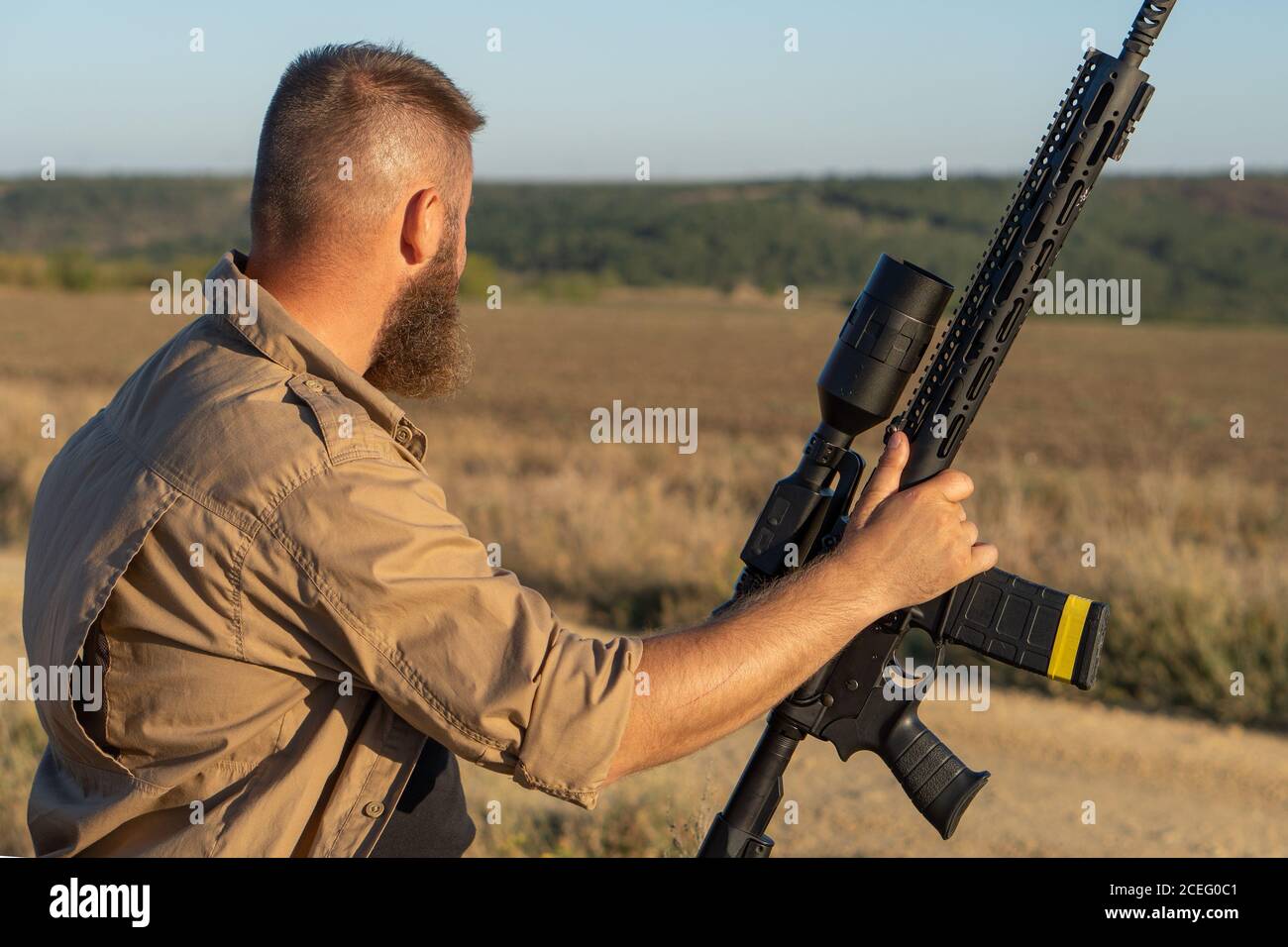 Un cacciatore con un'arma a caccia sullo sfondo di un bellissimo paesaggio estivo. Sparatutto che sospira nel bersaglio. L'uomo Bearded è sul Foto Stock