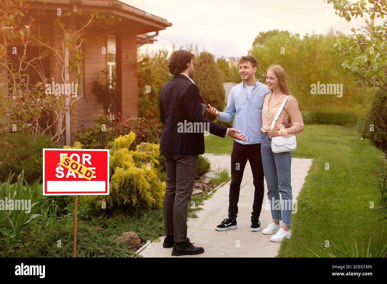 Broker immobiliare e nuovi proprietari di casa di fronte la loro proprietà all'aperto Foto Stock