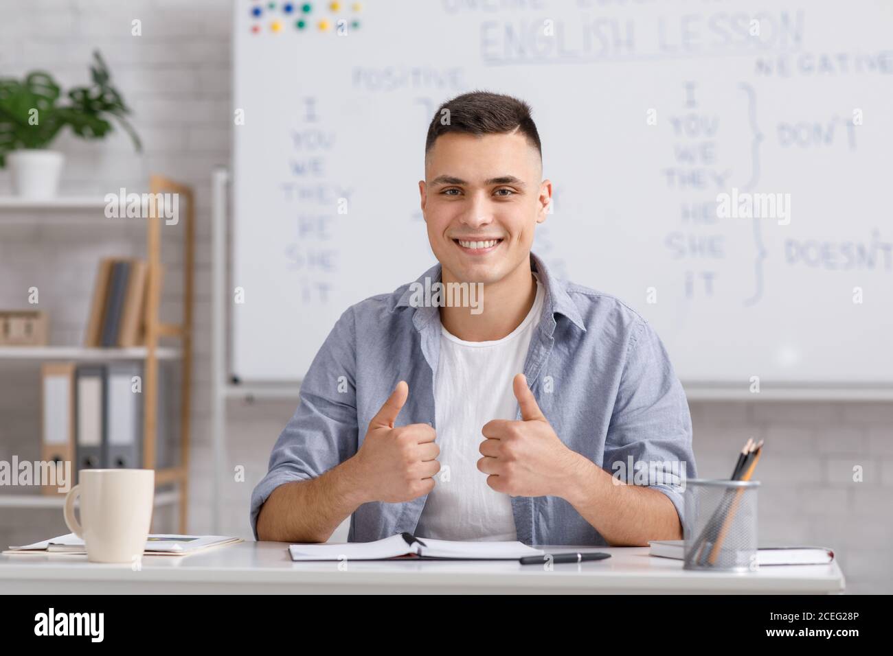 Lingua di apprendimento a distanza. Un giovane insegnante di sesso maschile sorridente che mostra i pollici e spiega agli studenti le regole inglesi Foto Stock