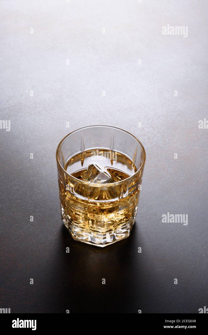 Un colpo di whisky con cubetto di ghiaccio su sfondo marrone scuro. Foto Stock