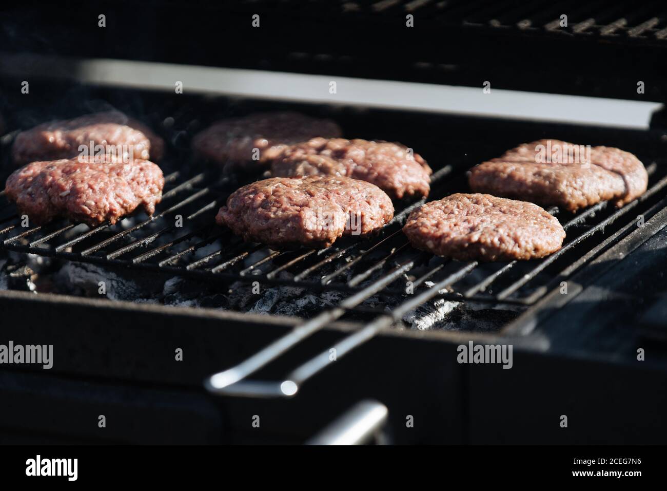 Poche frittatine di hamburger crudo arrostendo sulla griglia di barbecue all'esterno sotto la luce del sole Foto Stock