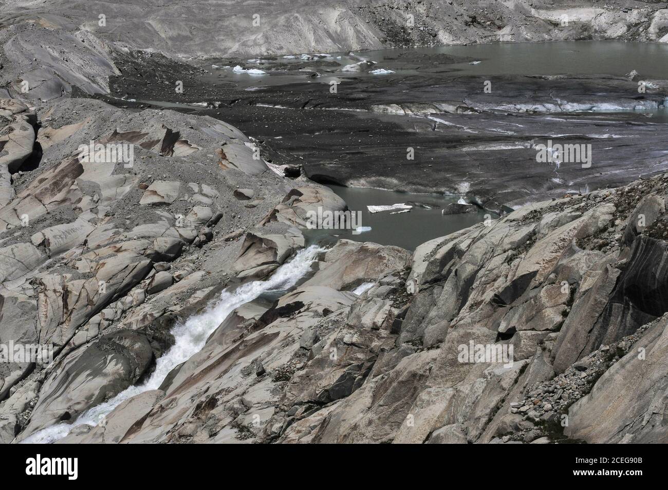 Gli scienziati del clima incolpano il riscaldamento globale per il retrattamento del ghiacciaio Rhône, sorgente del fiume Rhône, che si fonde ora in estate sotto il Passo Furka nel Cantone Vallese, Svizzera, a un'altitudine di circa 2,208 m (7,244 piedi). Nel 1850, una lingua di ghiaccio si estendeva bene lungo il fianco della montagna prima di fondersi nella valle sottostante. Il ghiacciaio scorre per 7.65 km (4.75 mi) dai campi innevati delle alte Alpi Urner a circa 30 - 40 m (100 - 130 piedi) all'anno. Il torrente che scorre dal lago d'acqua fusa inizia il viaggio del fiume di 813 km (505 mi) attraverso la Francia meridionale verso il Mediterraneo. Foto Stock