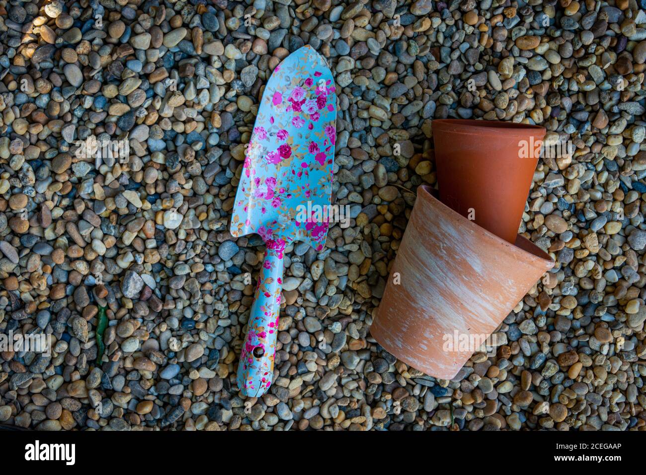 colorati utensili da giardino con vasi di fiori in terracotta su un sfondo ghiaia Foto Stock