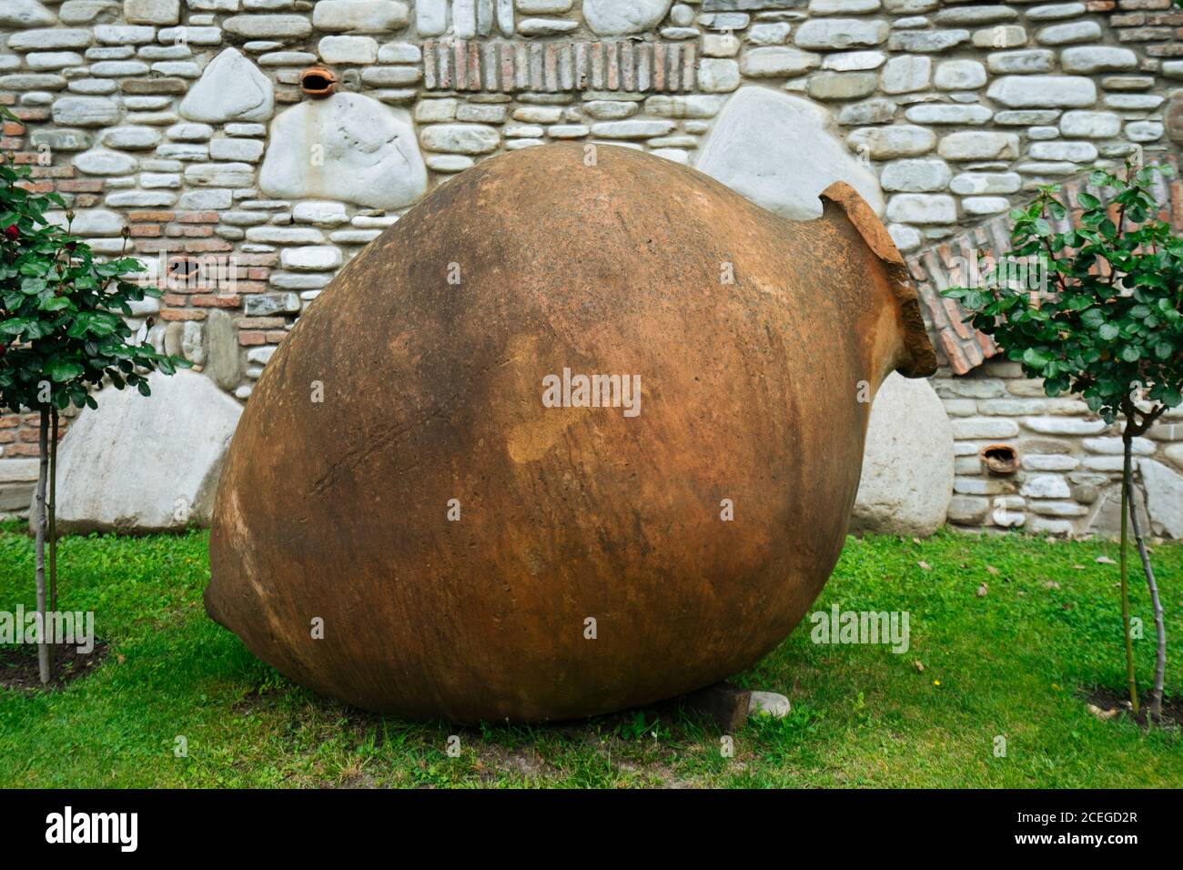 Tradizionale terracotta georgiana kvevri per la produzione di vino adagiato sull'erba tra piccole segature di alberi sullo sfondo di pietra bianca e. muro di mattoni Foto Stock
