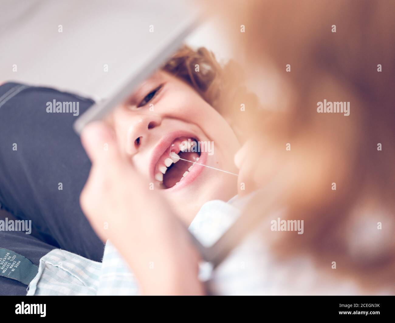 Crop ragazzino tenendo piccolo specchio e guardando in riflessione mentre si estrae il dente con la filettatura Foto Stock