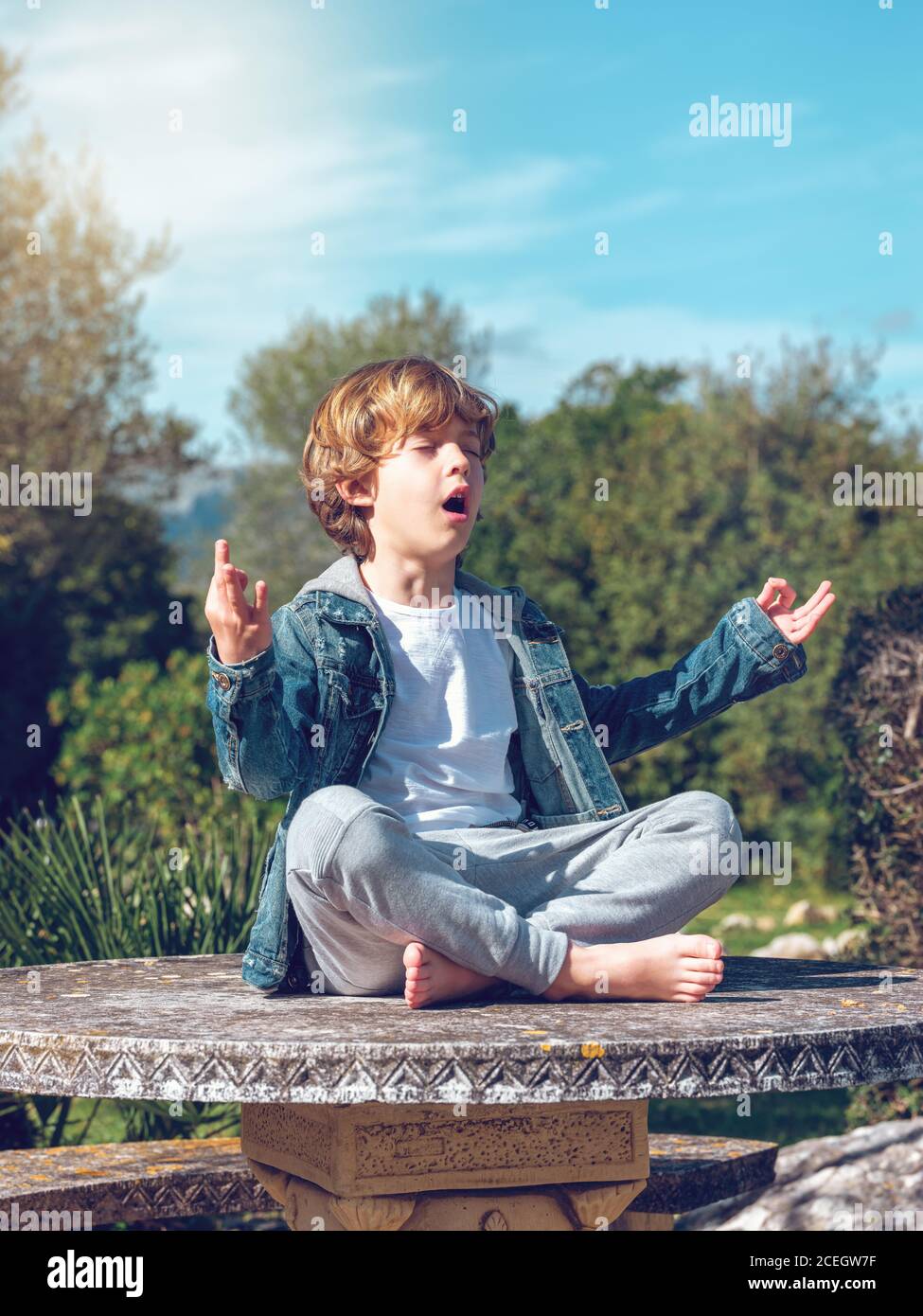 Adorabile ragazzino seduto e meditante in loto posa in una giornata di sole. Foto Stock