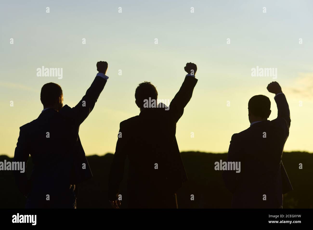 Business e concetto di successo. I leader discutono, tengono in mano il progetto. Silhouette di uomini in piedi contro il cielo della sera. I dirigenti che indossano abiti eleganti ammirano la vista. Foto Stock