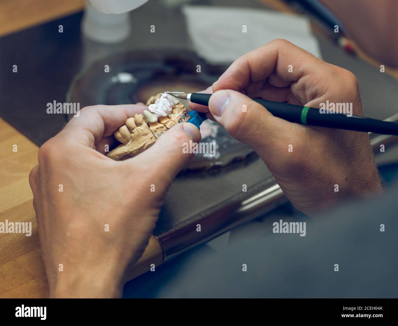 Coltivare il tecnico odontoiatrico utilizzando l'attrezzo speciale su cui applicare lo smalto formi dentiera mentre fa l'impiallacciatura in laboratorio Foto Stock
