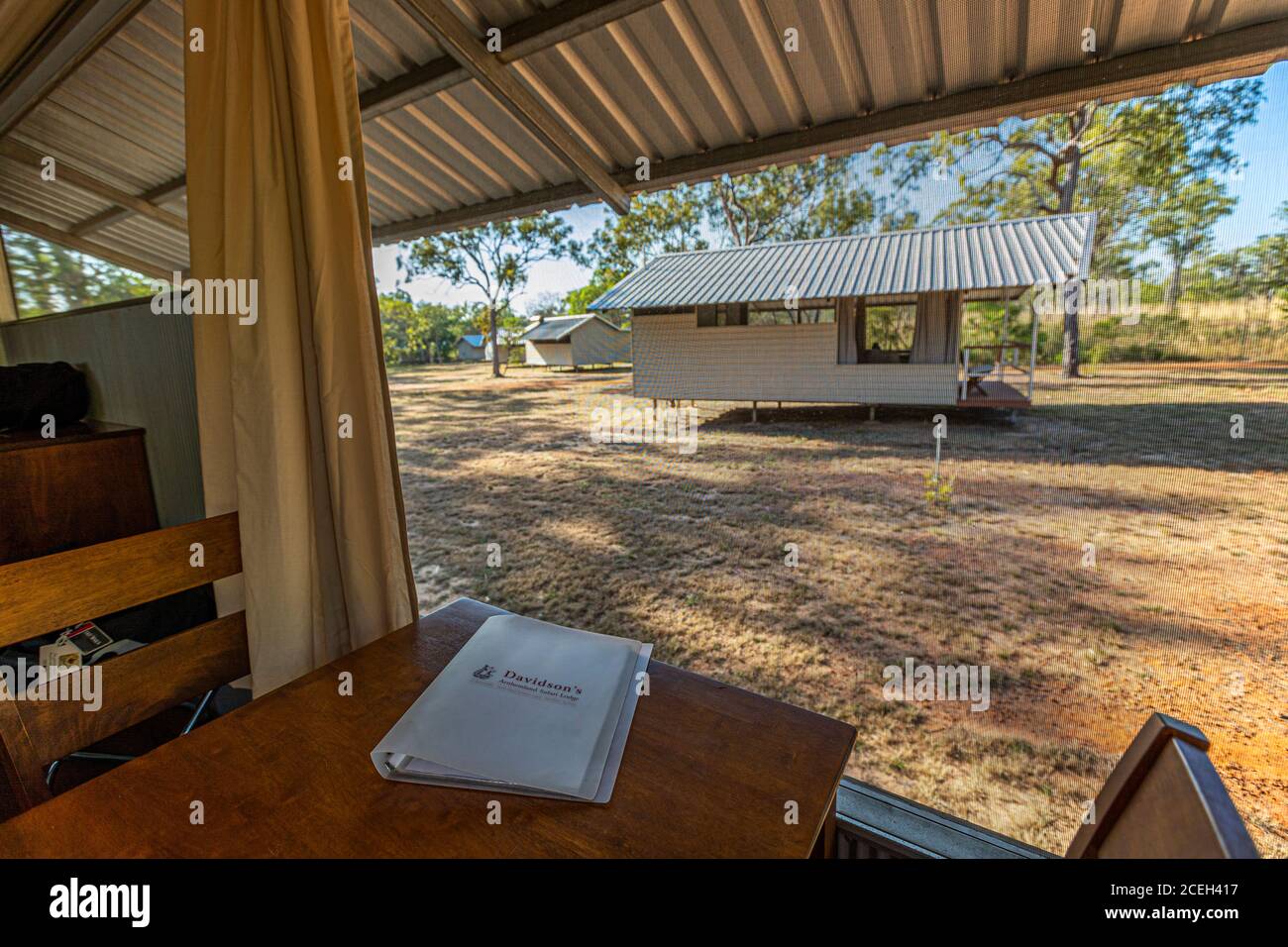 Una tenda per gli ospiti di Davidson's Arnhemland Safaris si affaccia sul prato verso una delle capanne della lodge vicino al Monte Borradaile, Territorio del Nord, Australia, con una cartella con il logo di Davidson's sul tavolo della veranda coperta. Foto Stock