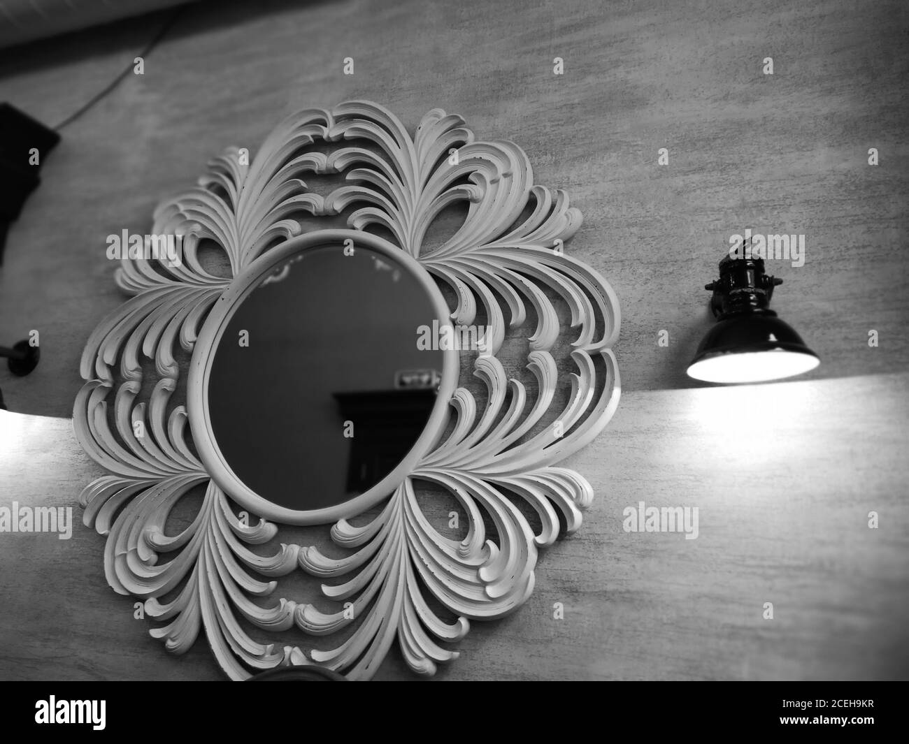 Uno specchio rotondo in una cornice di apertura e una lampada sulla parete. Dettagli in stile vintage. Fotografia in bianco e nero Foto Stock