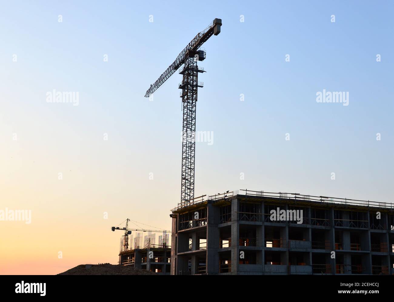 Sagome di gru a torre che costruiscono un nuovo edificio residenziale in un cantiere di costruzione sullo sfondo del tramonto. Programma di ristrutturazione, sviluppo, Foto Stock