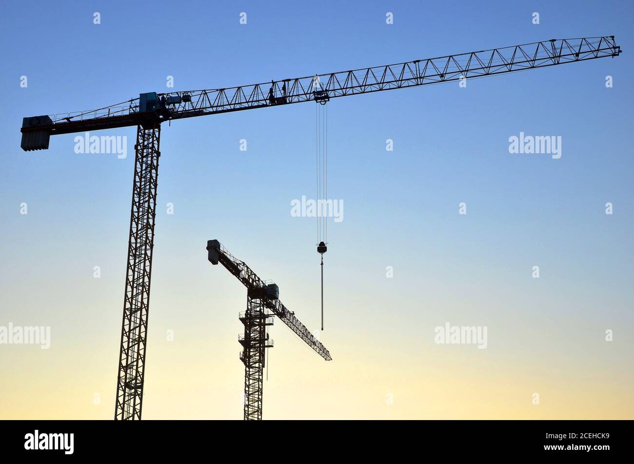 Sagome di gru a torre che costruiscono un nuovo edificio residenziale in un cantiere di costruzione sullo sfondo del tramonto. Programma di ristrutturazione, sviluppo, Foto Stock