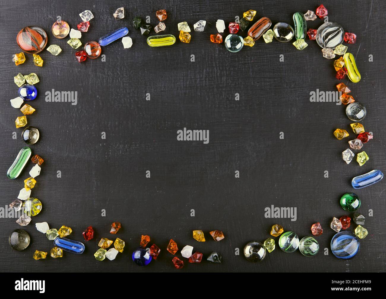 Sfere di marmo di vetro multicolore e ciottoli di vetro su superficie nera a forma di cornice. Pietre colorate di Mancala gioco a bordo Foto Stock