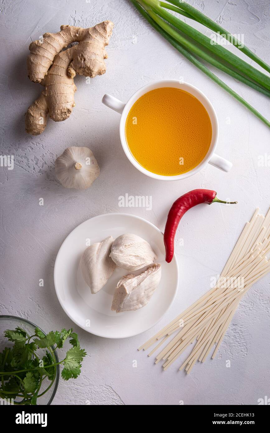 Ingredienti piccanti per zuppe asiatiche. Zenzero, aglio, brodo di pollo e carne, peperoncino rosso, coriandolo e scalione, tagliatelle giapponesi. tessuto bianco st Foto Stock