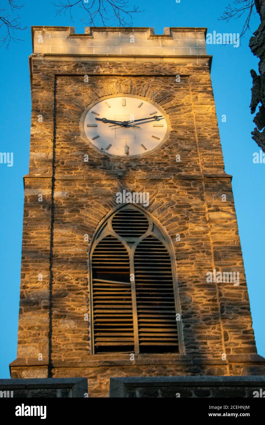 Un Clocktower bagnata dalla luce solare arancione e dalle ombre un albero Foto Stock