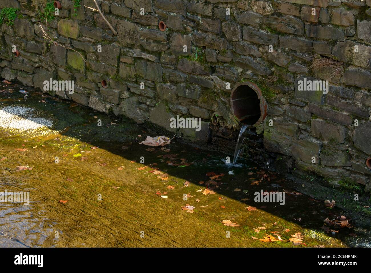 Un tubo di drenaggio in una parete di Cobblestone che versa in un Ruscello artificiale Foto Stock